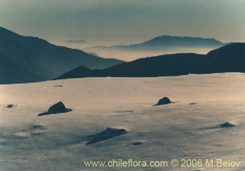 An image of a snow-covered mountain field, with large rocks, with Santiago below.