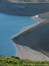 Image of volcanic ash slopes and the shore of Laguna Maule, with some green grass in foreground.