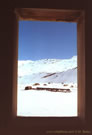 An image of a wooden window frame through which an iron bridge and snow-covered mountains can be seen, in the vicinity of Ba�os Morales and Ba�os de la Colina.